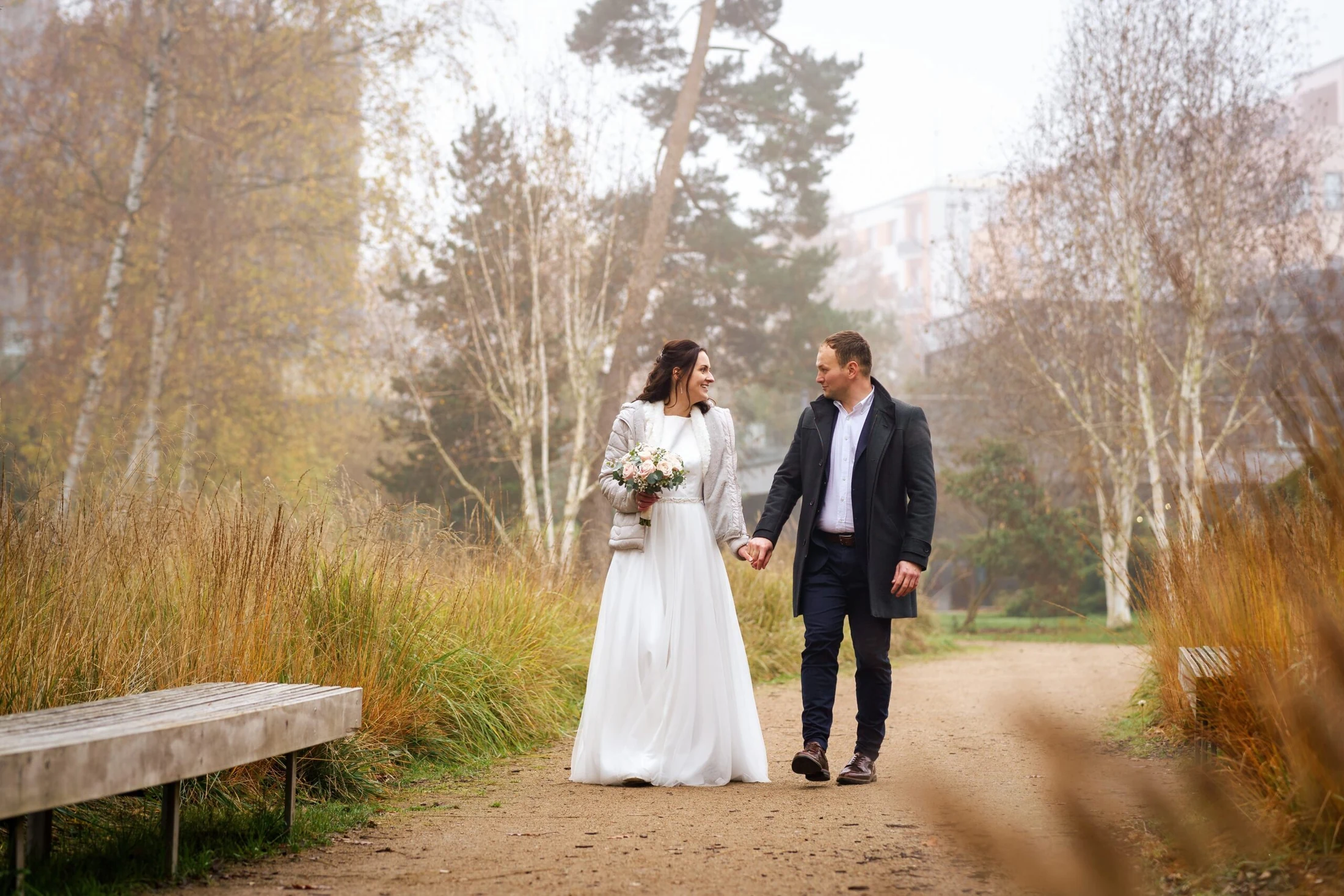Novomanželé jdou po cestě mezi břízami v podzimní mlze