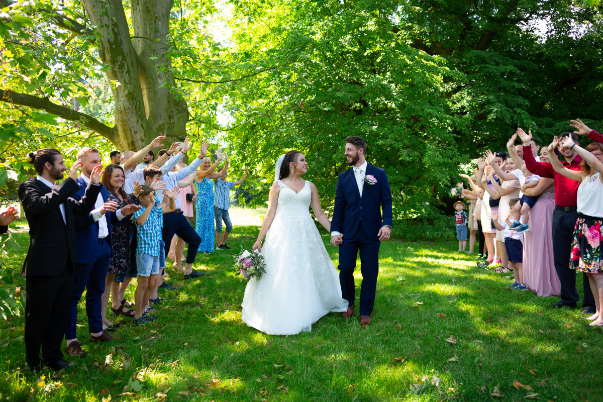 Nevěsta se drží se ženichem za ruce a prochází špalírem
